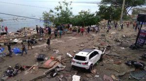 People walk past dead bodies (blue cover) a day after a tsunami hit Palu, on Sulawesi island on September 29, 2018. Rescuers scrambled to reach tsunami-hit central Indonesia and assess the damage after a strong quake brought down several buildings and sent locals fleeing their homes for higher ground. / AFP PHOTO / OLA GONDRONK