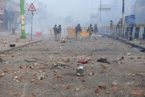 Policemen stand along a road scattered with stones as smoke billows from buildings following clashes between supporters and opponents of a new citizenship law, at Bhajanpura area of New Delhi on February 24, 2020, ahead of US President arrival in New Delhi. - Fresh clashes raged in New Delhi in protests over a contentious citizenship law on February 24, hours ahead of a visit to the Indian capital by US President Donald Trump. India has seen weeks of demonstrations and violence since a new citizenship law -- that critics say discriminates against Muslims -- came into force in December. (Photo by Sajjad HUSSAIN / AFP)