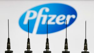 Medical syringes are seen with Pfizer company logo displayed on a screen in the background in this illustration photo taken in Poland on October 12, 2020. (Photo illustration by Jakub Porzycki/NurPhoto via Getty Images)