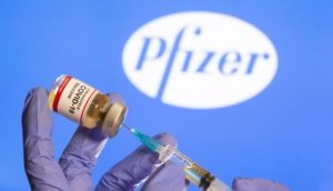A woman holds a small bottle labeled with a "Coronavirus COVID-19 Vaccine" sticker and a medical syringe in front of displayed Pfizer logo in this illustration taken, October 30, 2020. REUTERS/Dado Ruvic - RC29TJ9CENFB