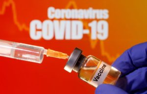 A small bottle labeled with a "Vaccine" sticker is held near a medical syringe in front of displayed "Coronavirus COVID-19" words in this illustration taken April 10, 2020. REUTERS/Dado Ruvic/Illustration/File Photo