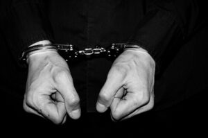 Handcuffed hands of arrested criminal man in black shirt and handcuffs